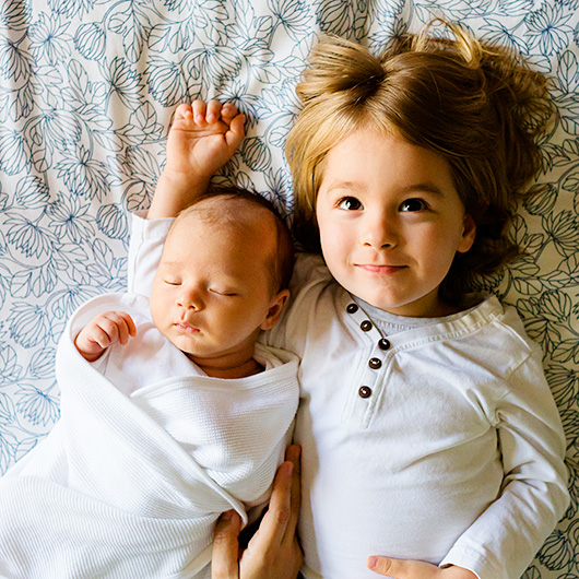 Kleinkind mit neugeborenem Geschwister auf einem Bett