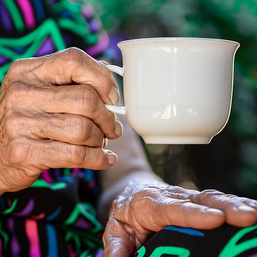 Hand einer alten Dame hält eine Kaffeetasse